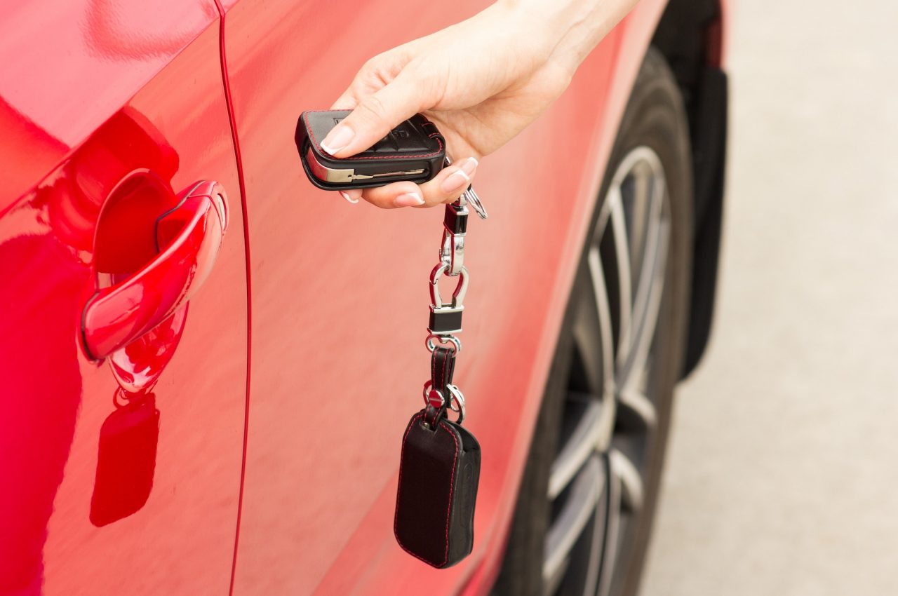 Hand pressing a car key remote beside a red car